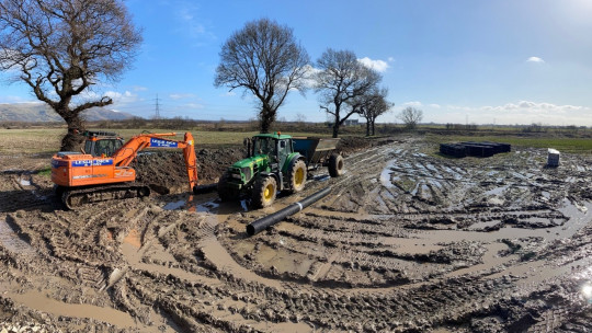 Digger and gravel cart with pipe in the background